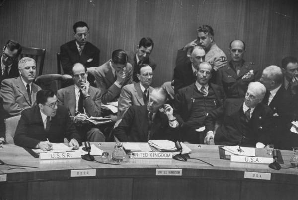 A meeting of the UN Atomic Energy Commission in October 1946. Bernard Baruch is the white-haired man sitting at the table at right behind the “U.S.A” plaque. At far top-right of the photo is Robert Oppenheimer. Two people above Baruch, in the very back, is General Groves. Directly below Groves is Manhattan Project scientist Richard Tolman. British physicist James Chadwick sits directly behind the U.K. representative at the table.